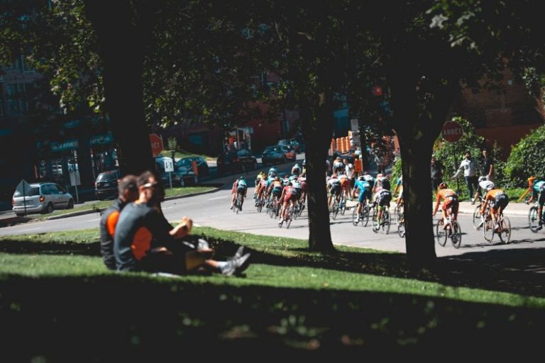 Economic Cycles - men sitting on grass field near trees and street with men in bike marathon